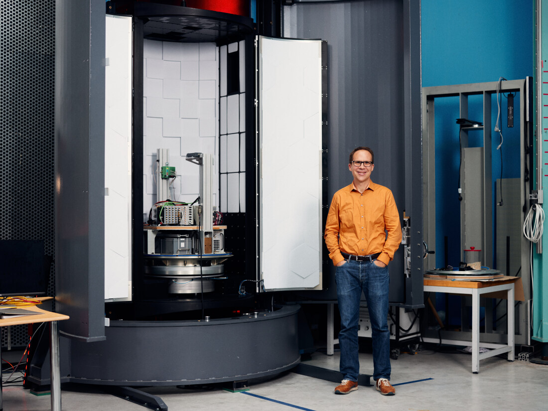 Marc Avila stands next to the “GraviTower Bremen Pro”, a large, gray tube, opened at the front, with an experiment carrier on a slide system inside.