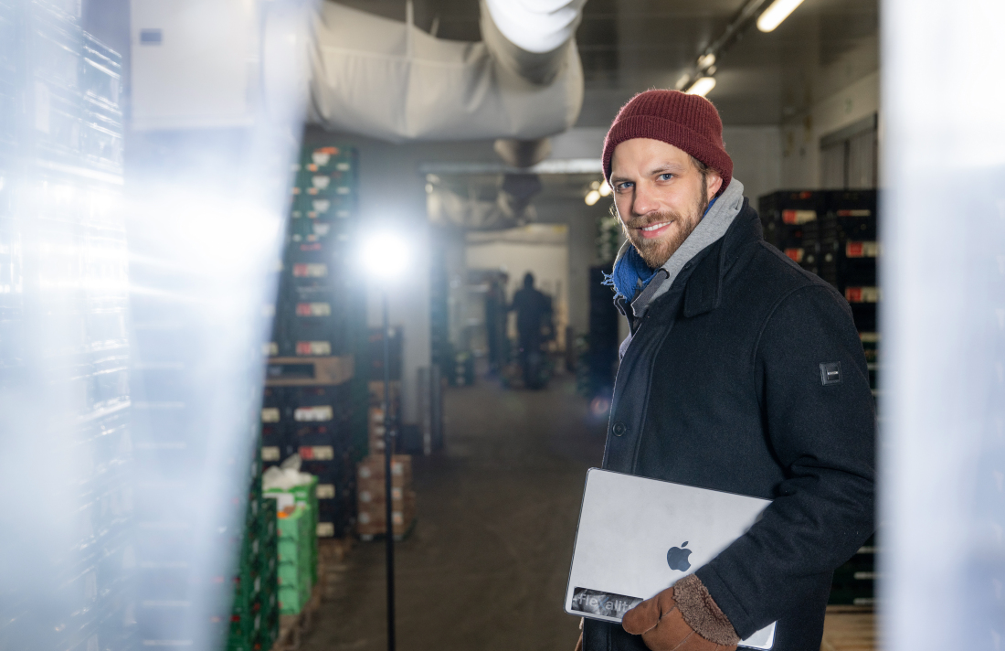 Dyke Wilke steht mit einem Laptop in einem Kühlhaus und lächelt in die Kamera.