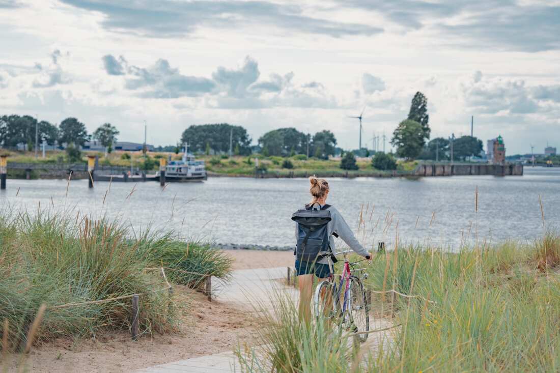 Eine Frau mit Fahrrad steht am Wasser